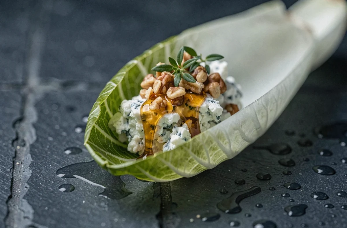 Gros plan d'une feuille d'endive garnie de fromage bleu crémeux, noix et miel sur ardoise noire